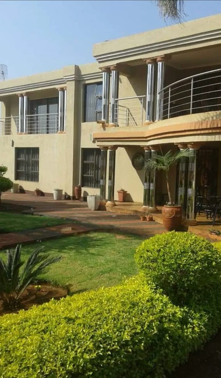 Double-storey home with curved stainless steel balcony balustrades and stainless steel pillar covering, behind a garden