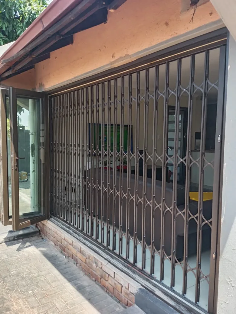 Bronze retractable burglar proofing closed across a wide opening beside an open aluminium folding door