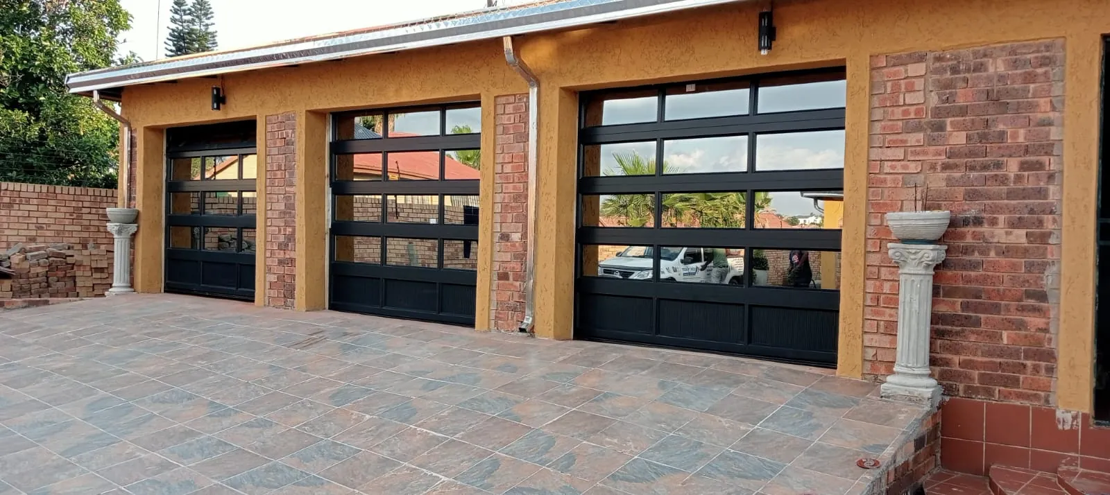Three single charcoal aluminium and glass garage doors on a face-brick home