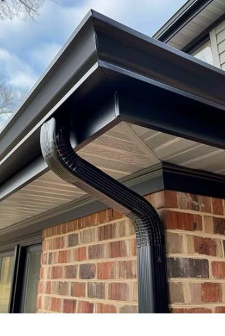 Example of a black seamless gutter with a matching black downpipe at the corner of a brick home