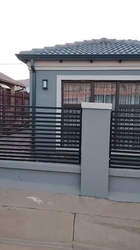 Grey home with dark gutters and a downpipe behind a slatted boundary fence