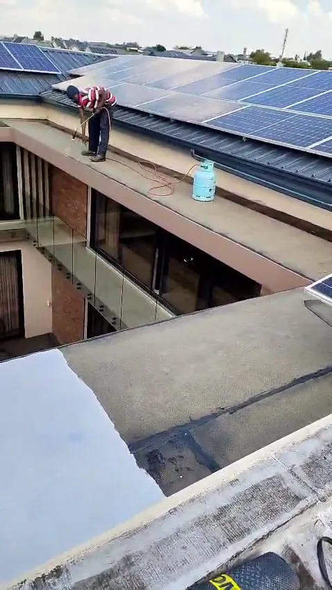 Waterproofing team member working on a roof with solar panels, above newly waterproofed parapets